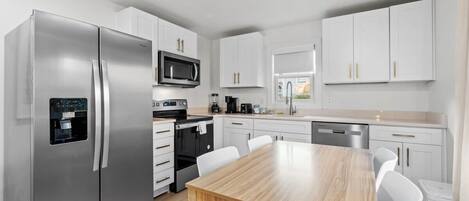A modern kitchen with white cabinets, stainless steel appliances, and a wooden dining table.