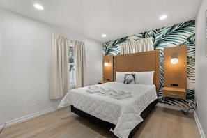 Ein Schlafzimmer mit einem Bett, Vorhängen, einer Wand mit einem Blattmuster und zwei Nachttischlampen.