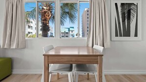 Un área de comedor moderna con una mesa de madera y sillas blancas, una ventana con cortinas y una obra de arte enmarcada en la pared.