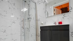 A modern bathroom with a glass-enclosed shower, a black cabinet, and a marble-tiled wall.
