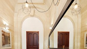 A long, dark wooden reception desk with a large mirror above it, flanked by two wooden doors and a bench with a patterned cushion.