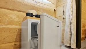 A compact refrigerator with a freezer compartment, located in a room with wooden walls and a tiled floor.