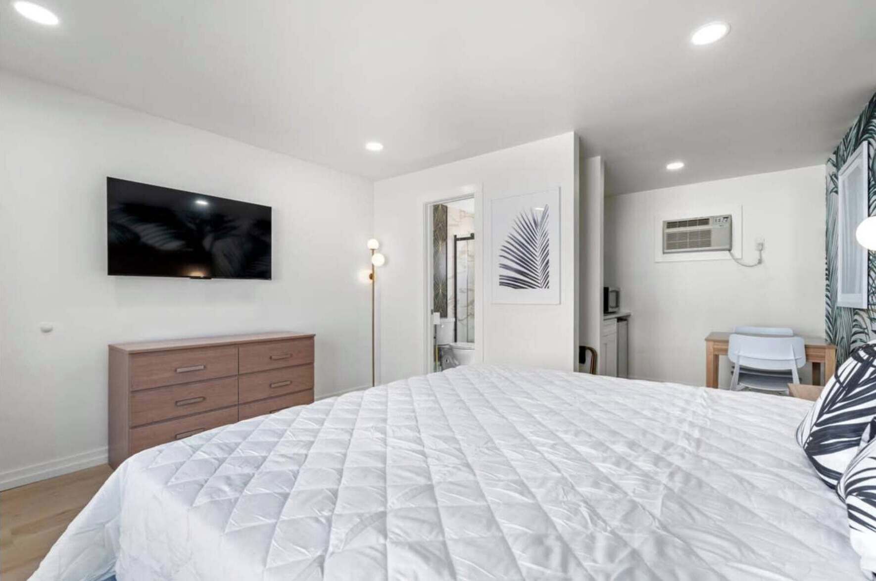 Un dormitorio moderno con una cama grande, un aparador, un televisor de pantalla plana y un escritorio con silla.