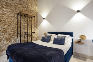 A bedroom with a stone wall, a bed with a dark headboard, and two wall-mounted lights. - Apartment 'Bella Encantada' with Wi-Fi and Air Conditioning (Cádiz)
