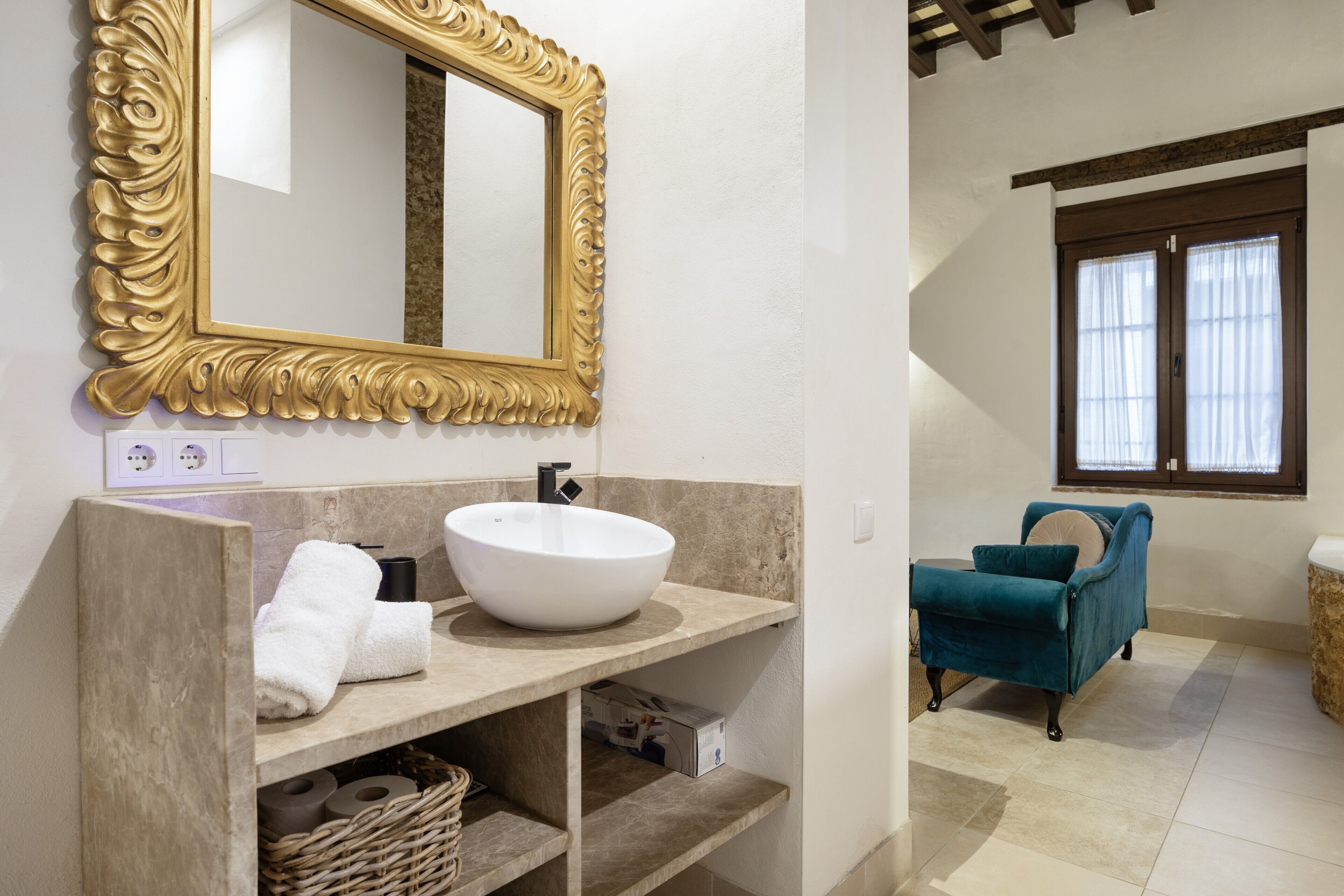 A bathroom with a large mirror, a white sink, and a blue chair.