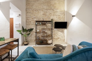 A living room with a brick wall, a mounted TV, a blue sofa, a wooden table, and a potted plant. - Apartment 'Bella Encantada' with Wi-Fi and Air Conditioning (Cádiz)