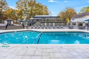 Ein Swimmingpool mit Liegestühlen und einem überdachten Bereich, umgeben von Bäumen und einem Gebäude mit Beschilderung.
