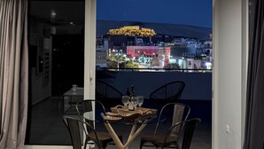 A balcony with a table set for two, overlooking a cityscape with illuminated buildings and a hill. - Acropolis Magical View Suite, Metro Kerameikos (Athens)