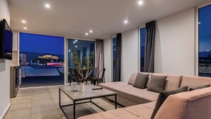 A modern living room with a sofa, a coffee table, and a dining area with chairs and a plant. - Acropolis Magical View Suite, Metro Kerameikos (Athens)