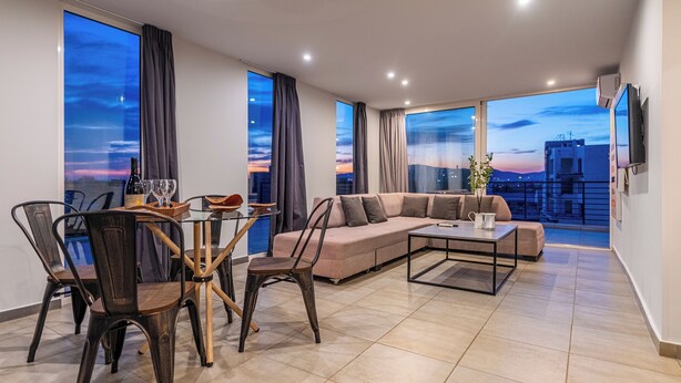A modern living room with a sofa, dining table, chairs, and large windows with curtains. - Acropolis Magical View Suite, Metro Kerameikos (Athens)