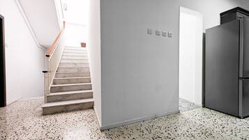 A modern kitchen with a stainless steel refrigerator, a staircase leading to a bright area, and a speckled floor.