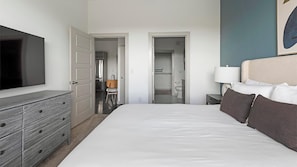 A hotel room with a large bed, a dresser, a TV, and a bathroom visible through an open door. - Landing | Amazing 1BD, Pool, Gym (Allen)