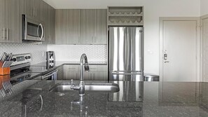 A modern kitchen with stainless steel appliances, a granite countertop, and wooden cabinets. - Landing | Amazing 1BD, Pool, Gym (Allen)