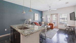Una cocina moderna con una isla de mármol, un comedor con una trona y una sala de estar con sofá y mesa de centro.