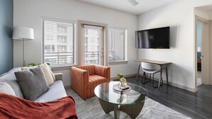 Una sala de estar moderna con sofá, sillón, mesa de centro de vidrio y televisor montado en la pared.