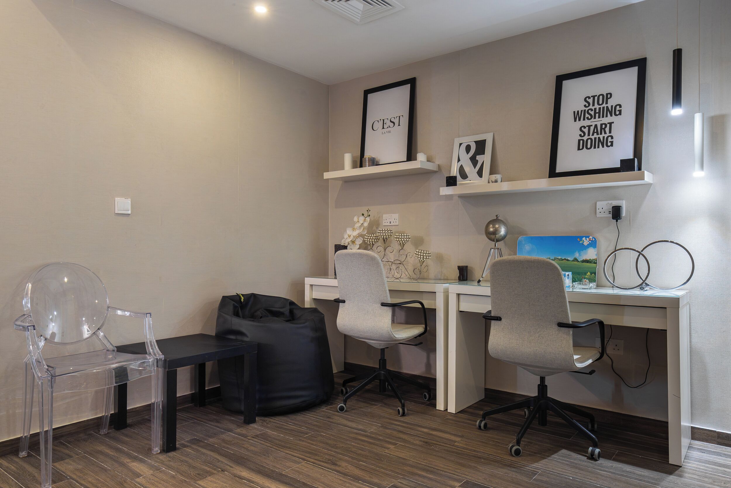 Un espacio de oficina moderno con un escritorio, dos sillas de oficina, una silla de plástico transparente, un bolso negro y decoración de pared motivacional.