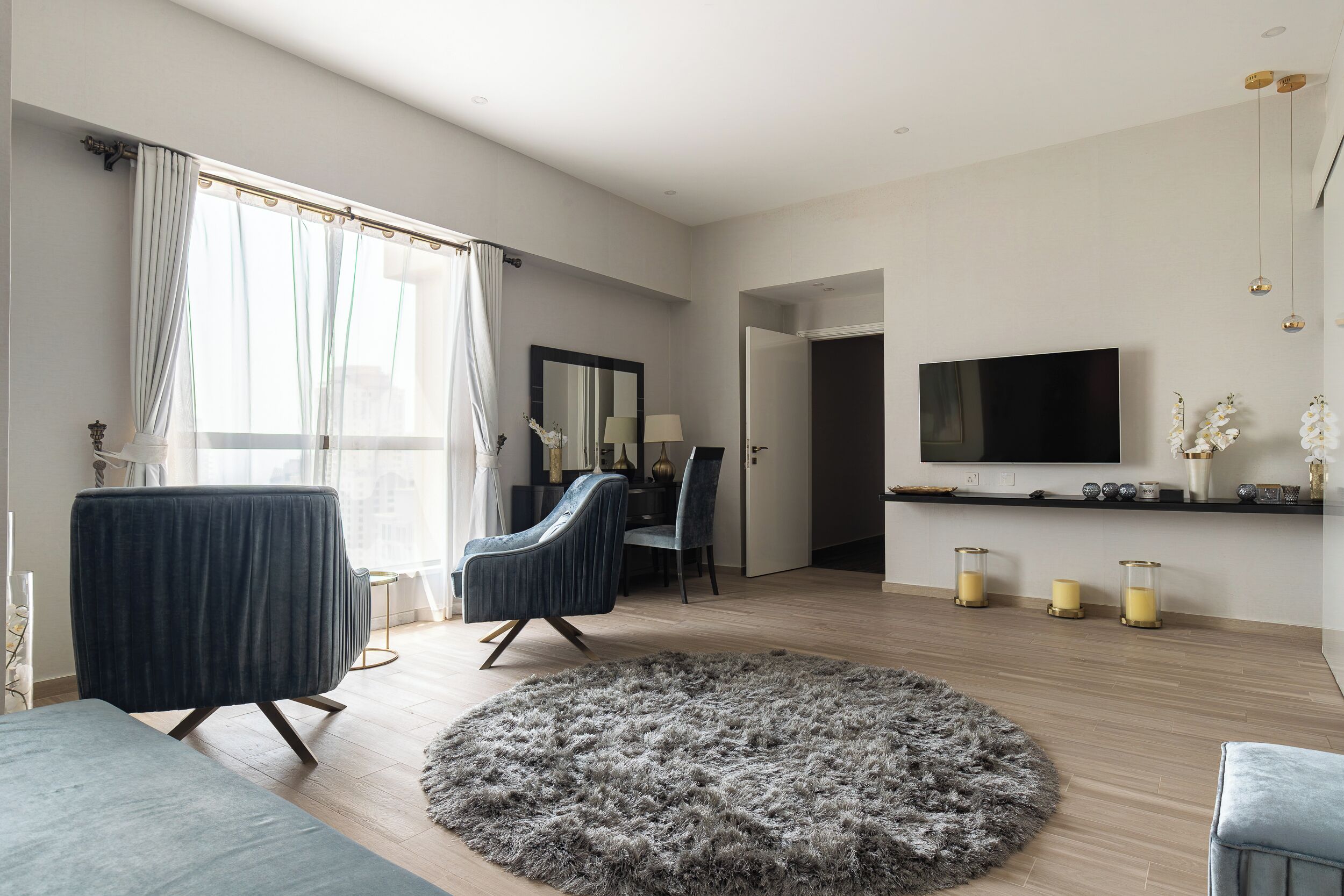 Ein modernes Wohnzimmer mit großem Fenster, einem Flachbildfernseher, einem runden Teppich und einem Essbereich mit Stühlen.
