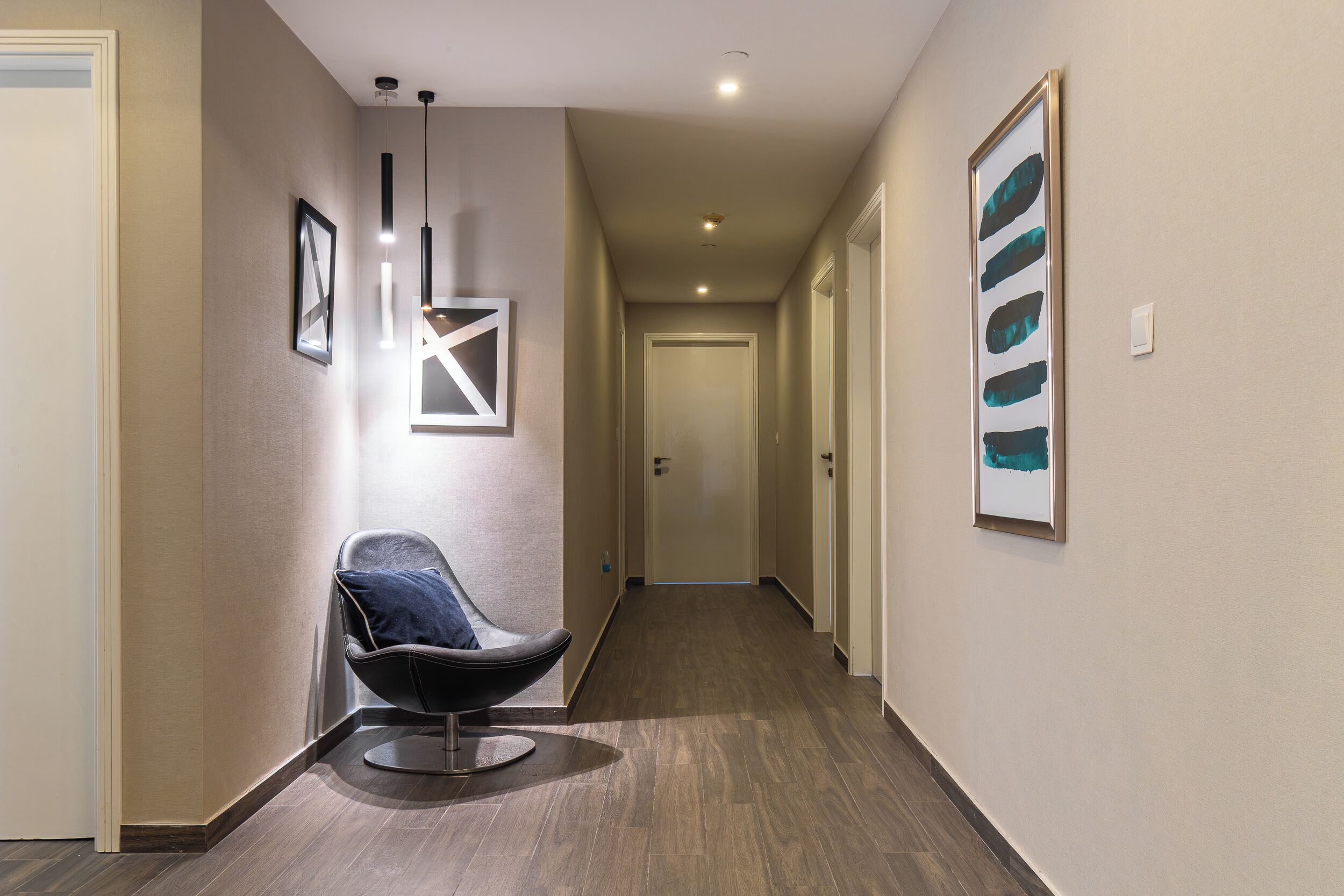 A hallway with a modern chair, framed artwork, and recessed lighting.