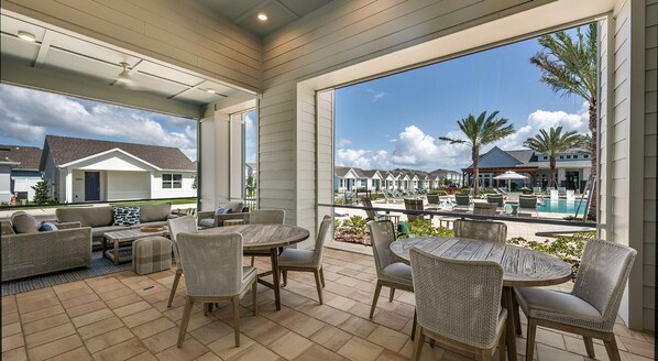 A covered patio with wicker furniture, a pool area with lounge chairs, and a view of a residential neighborhood. - Landing Apartments - Four Corners (Kissimmee)