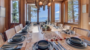 Ein Esszimmer mit einem langen Tisch, gedeckt für eine Mahlzeit, großen Fenstern mit Bergblick und einer Kristallleuchter.