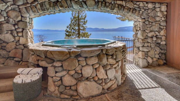 Ein mit Steinen umrahmter Whirlpool mit Blick auf einen See und Berge.