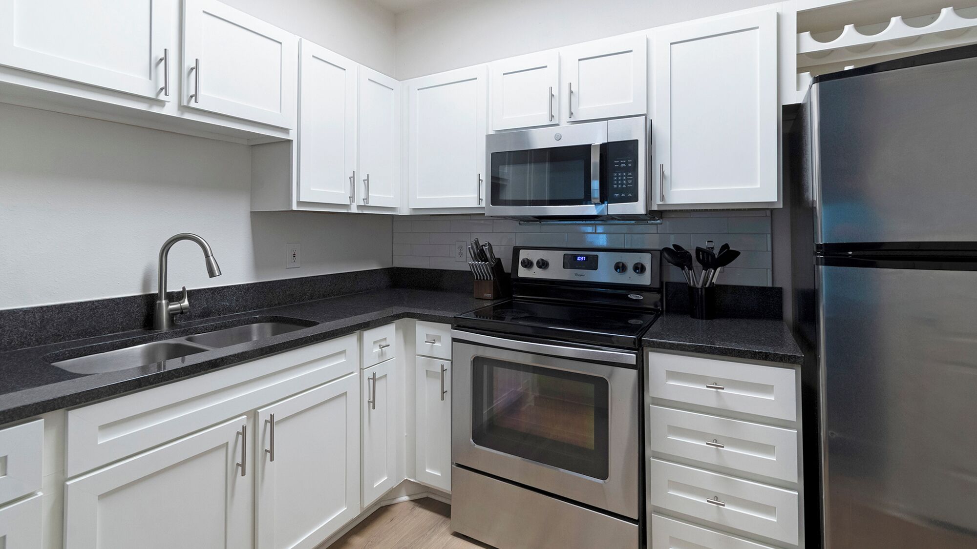 A modern kitchen with white cabinets, stainless steel appliances, and a black countertop.
