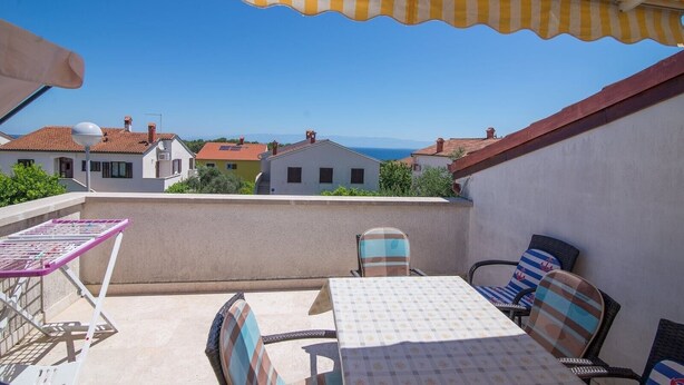 Un balcon avec une table et des chaises, un auvent à rayures et une vue sur les maisons et la mer.