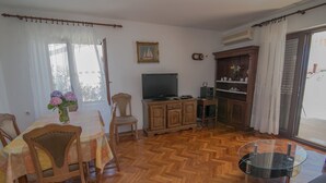 Un salon doté d’un parquet en bois disposé en motif à chevrons, d’une table à manger avec des chaises, d’un téléviseur, d’un meuble et d’une table basse en verre.