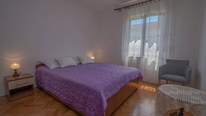 Une chambre à coucher avec un lit, une table de chevet, une chaise et une fenêtre avec des rideaux.