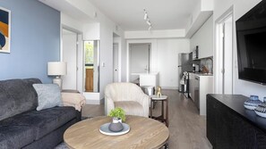 Ett modernt vardagsrum med en soffa, ett soffbord och en tv. Det finns också ett köksutrymme med en mikrovågsugn och ett kylskåp.