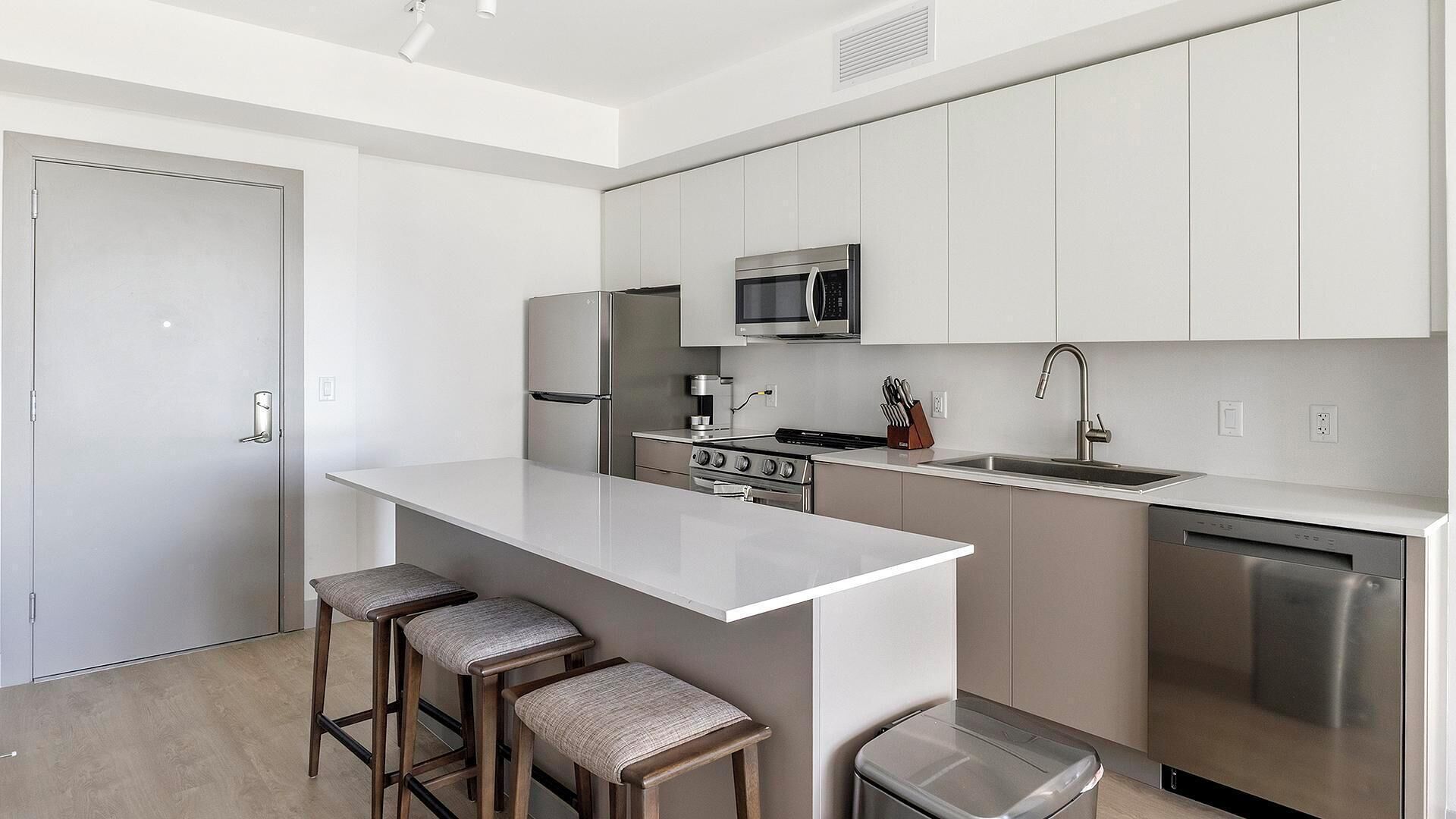 Cozinha moderna com ilha central, eletrodomésticos de aço inoxidável e banquetas de bar.