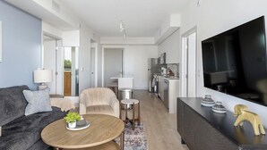 Ett modernt vardagsrum med en soffa, ett soffbord och en tv. Det finns också ett köksområde med ett kylskåp och en mikrovågsugn.