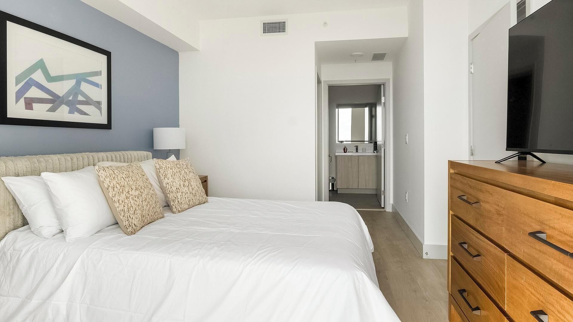 Une chambre d’hôtel avec un lit, une télévision, une commode et une salle de bain visible à travers une porte ouverte.