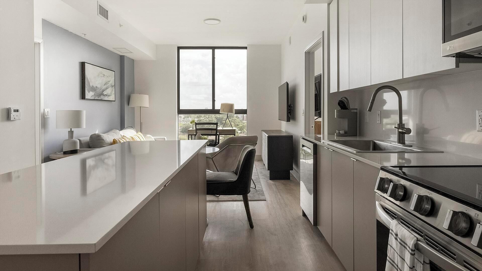 A modern kitchen with a central island, a dining area with a table and chairs, and a large window providing natural light.