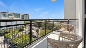 Un balcon donnant sur un parking et des immeubles, avec deux fauteuils en osier.