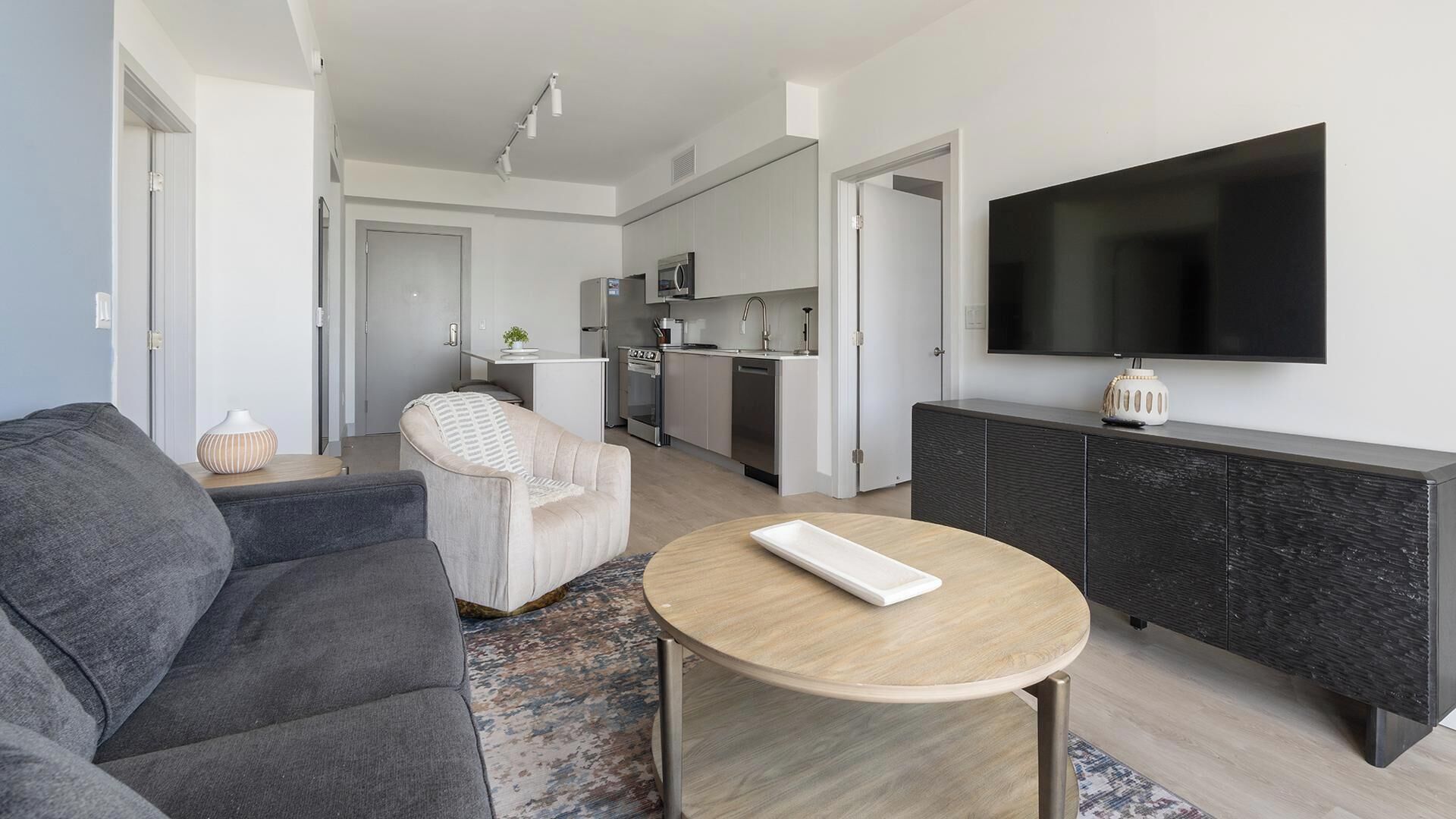 A modern living room with a grey sofa, a round coffee table, and a TV mounted on the wall.