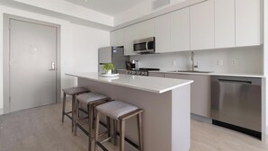 Een moderne keuken met een centraal eiland, barstoelen, roestvrijstalen apparatuur en een vaatwasser.