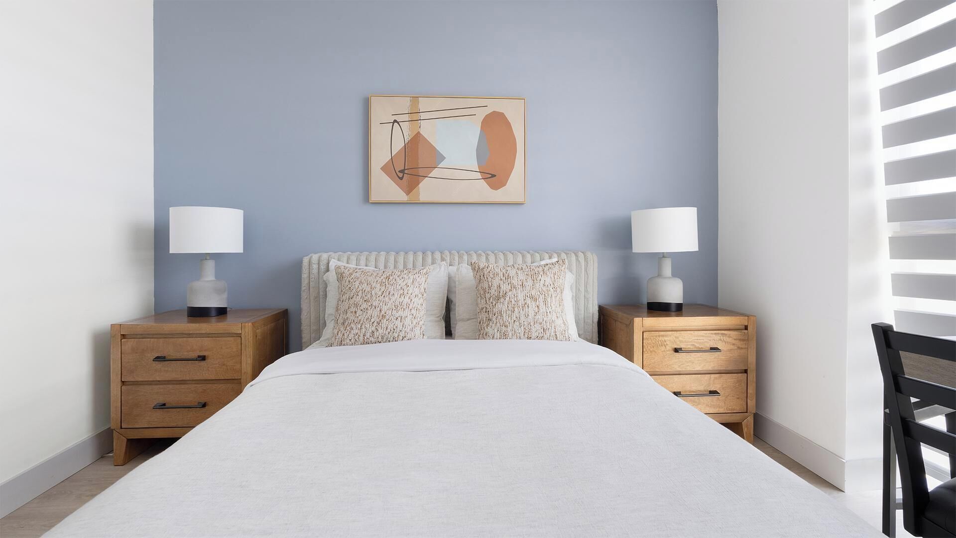 Una camera da letto con un letto, due comodini con lampade, un quadro astratto appeso al muro e una finestra con persiane.