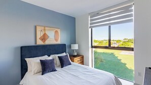 Une chambre à coucher avec un grand lit, une table de chevet, une lampe et une vue sur un paysage verdoyant par la fenêtre.