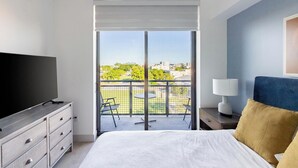 Une chambre d’hôtel avec un grand lit, un téléviseur posé sur une commode, un balcon offrant une vue sur la ville et une petite table avec une lampe.