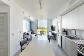 A modern kitchen with white cabinets, a built-in oven, and a large window offering a view of greenery. - Landing | Stunning 2BD, Gym, Clubhouse (North Miami)