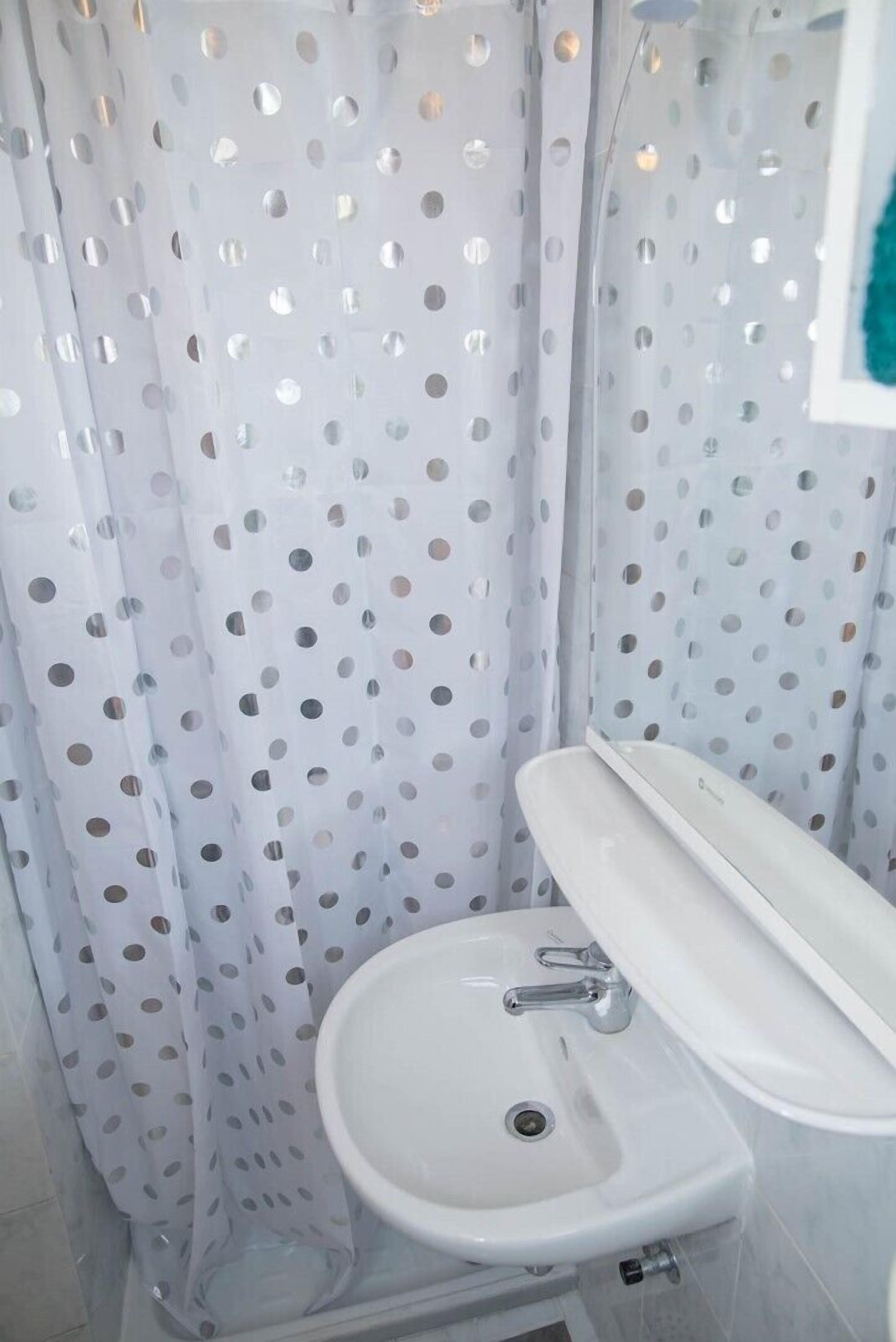 Une salle de bain avec un lavabo blanc et un rideau de douche à motifs à pois.