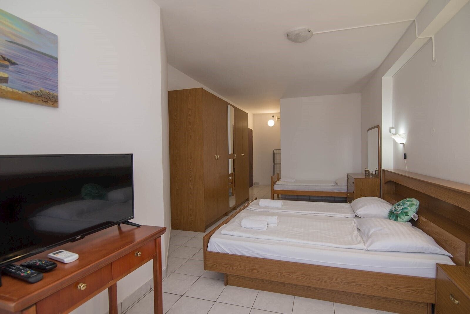 Ein Hotelzimmer mit einem Bett, einem Fernseher, einem Schreibtisch mit Fernbedienung und einem Kleiderschrank.
