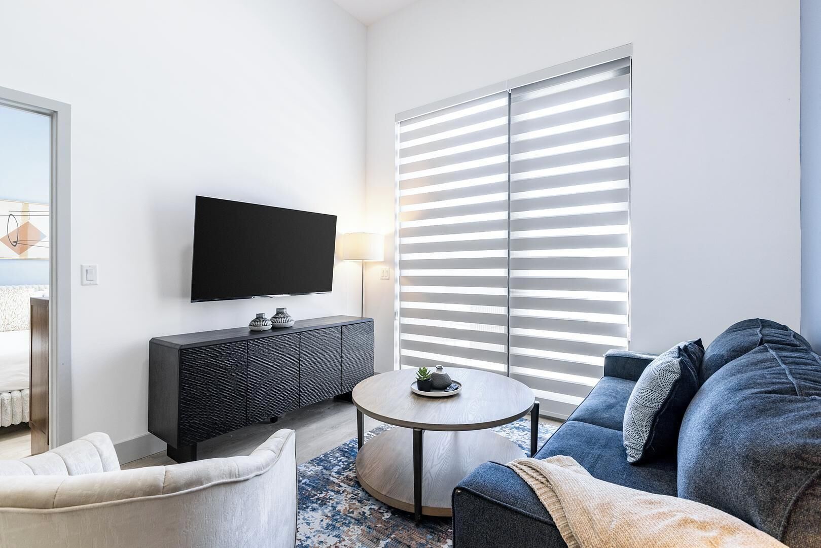 A modern living room with a flat-screen TV, a dark console, a round coffee table, and a blue sofa.