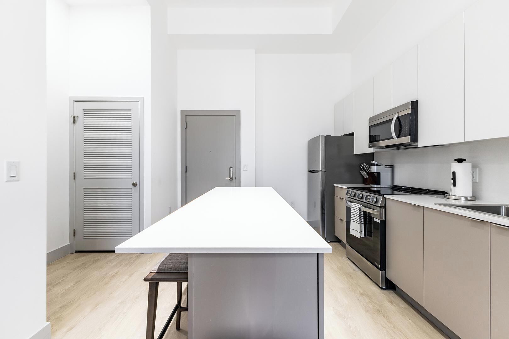 Una cocina moderna con una isla central, electrodomésticos de acero inoxidable y suelo de madera clara.