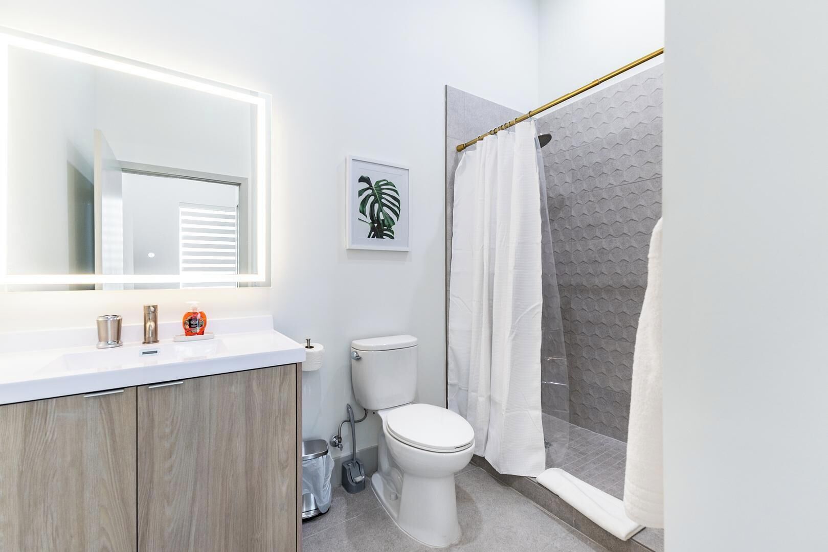 Une salle de bain moderne avec un meuble-lavabo en bois, un grand miroir, des toilettes et une douche avec un mur à texture.