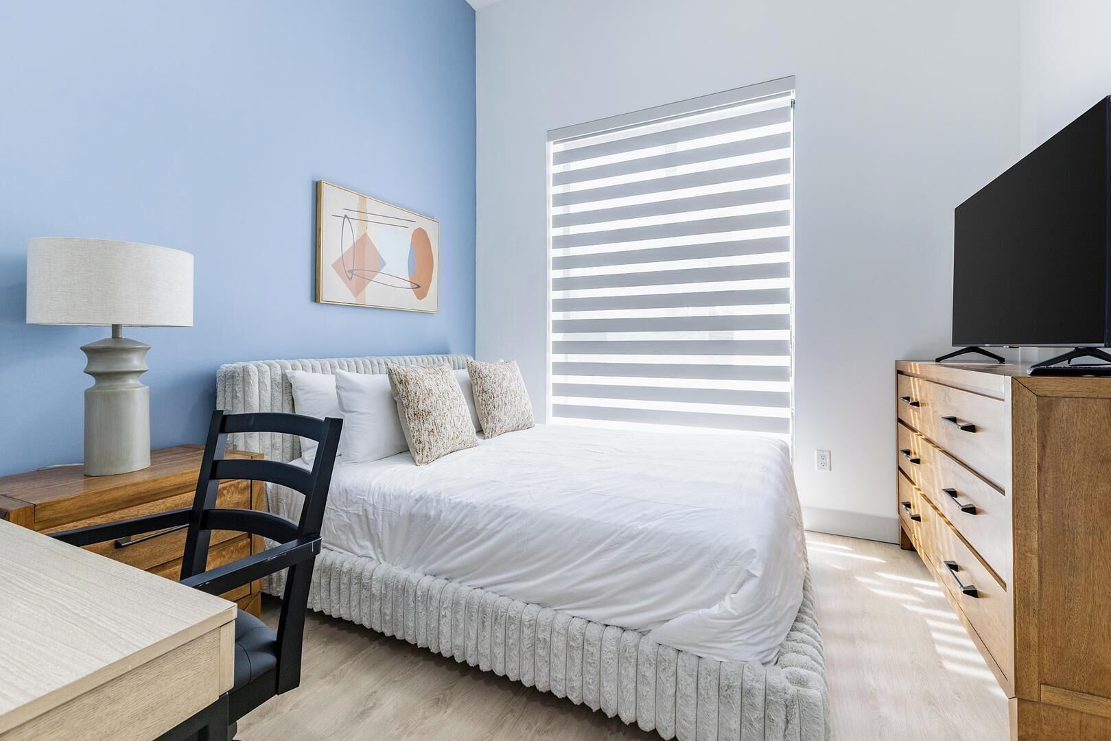 Une chambre à coucher comprenant un lit, un bureau, une chaise, une commode et un téléviseur.