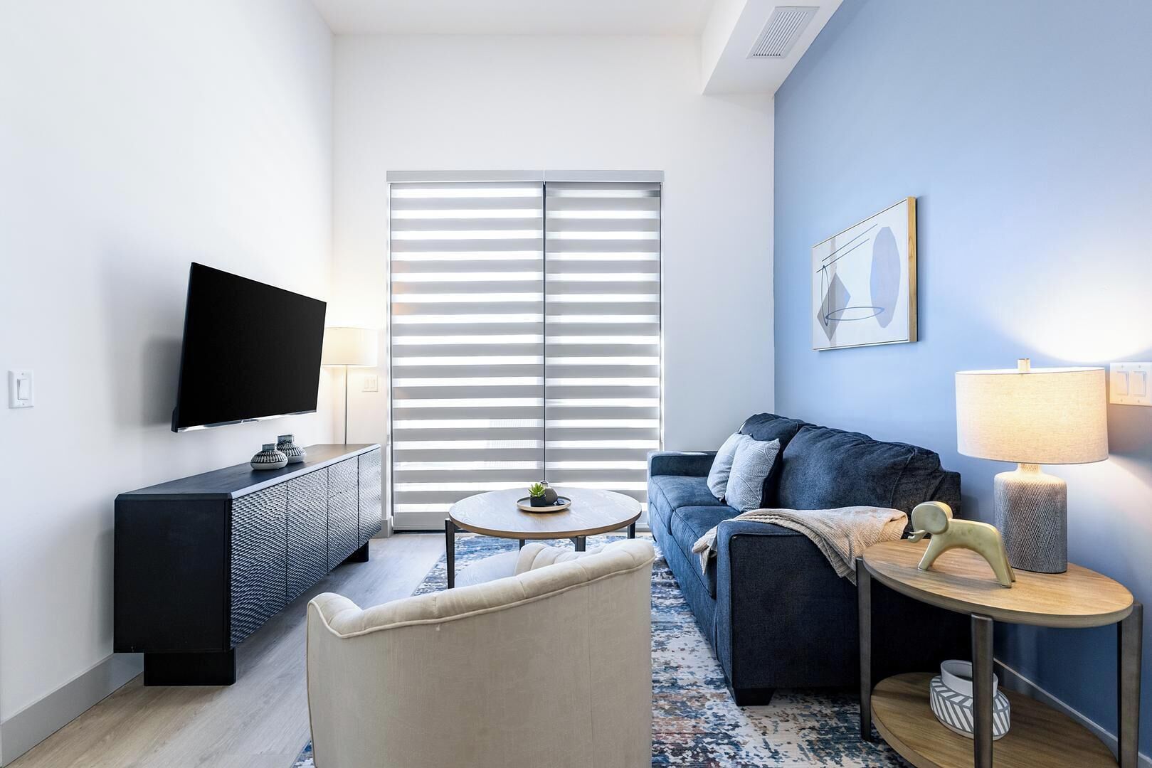 Ein modernes Wohnzimmer mit Flachbildfernseher, einer Couch, einem Couchtisch und einer Lampe.