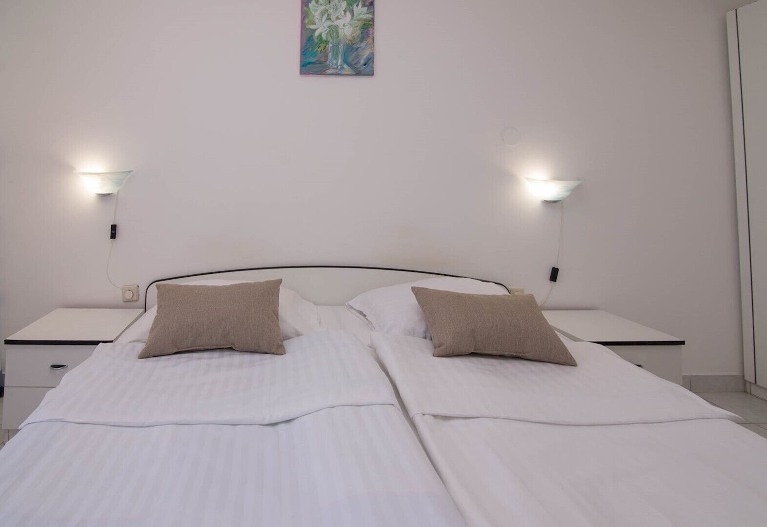 A double bed with two pillows, a bedside table, a wall-mounted light, and a painting above the bed.