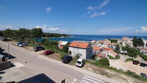 A coastal village with a road, parked cars, and buildings with red-tiled roofs. - Sv. Martin / B&B sv Martin C, pogled na more (Mali Lošinj)
